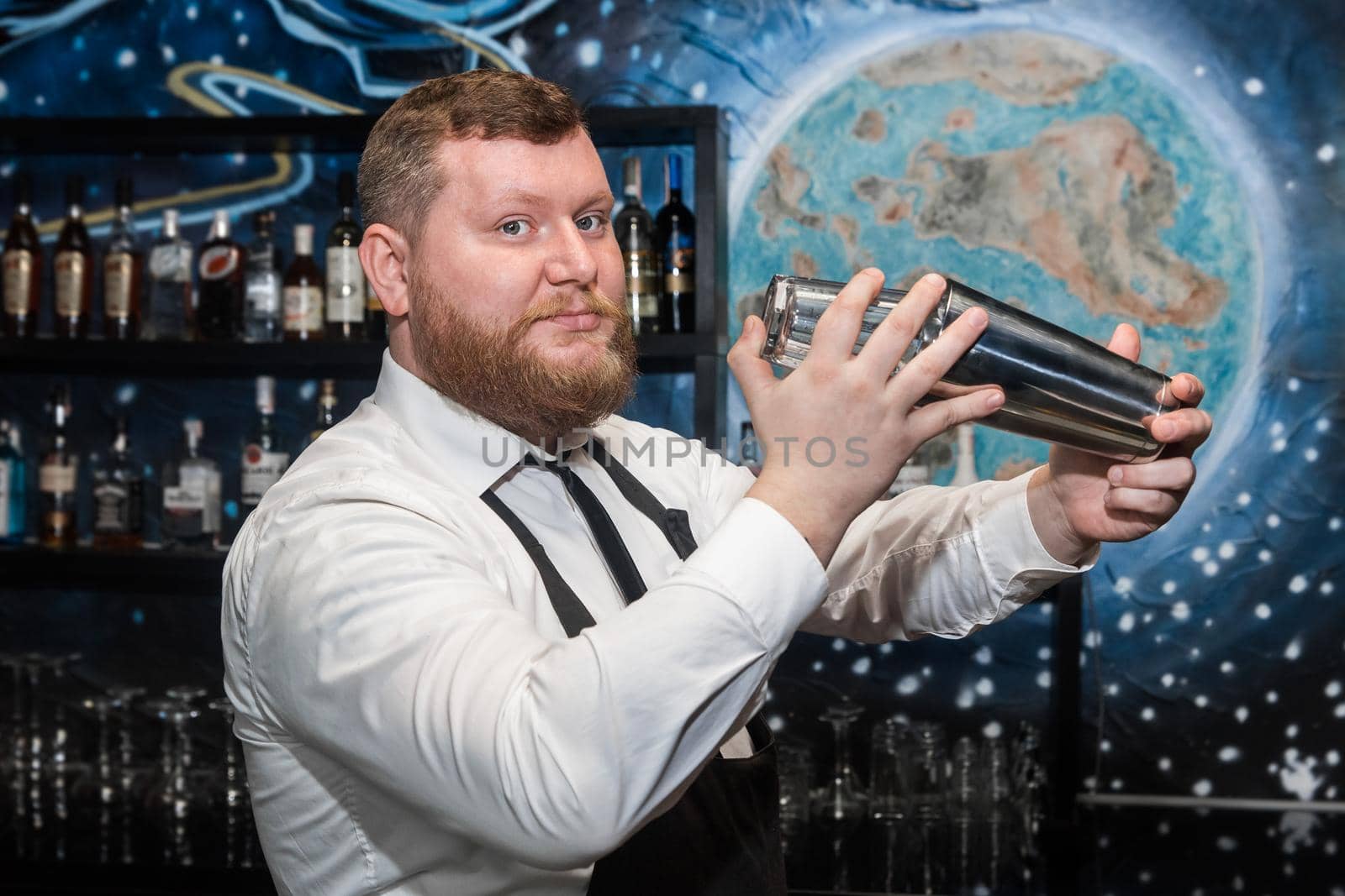 Hands of a professional adult bearded Caucasian man bartender beat and mix ingredients in a tool for making alcoholic cocktails with a metal shaker.