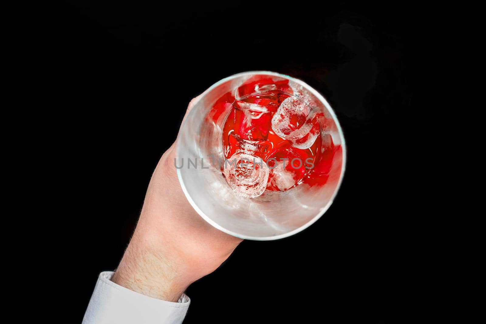 The hand of professional bartender takes a tool for mixing and making alcoholic cocktails shaker with red cold syrup with ice in on a black background, close-up.