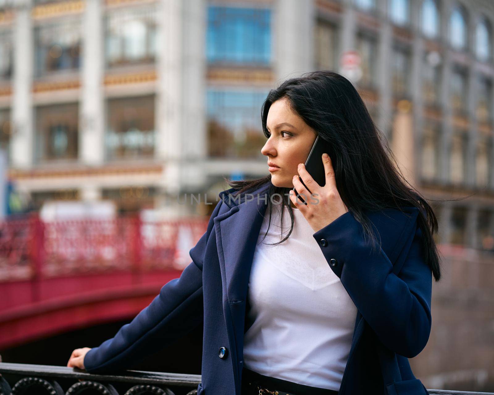 Woman with long hair talking on phone. Autumn or winter, girl in outdoor. Beautiful intelligent brunette in street of Saint-Petersburg in a city center near bridge, copy space