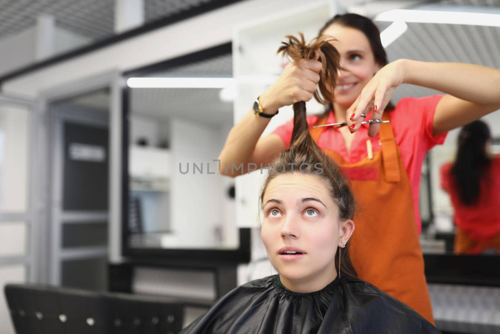 Portrait of hairdresser going to cut lock of long hair with scissors tool, female client scared in masters chair. Beauty salon, barbershop, image concept