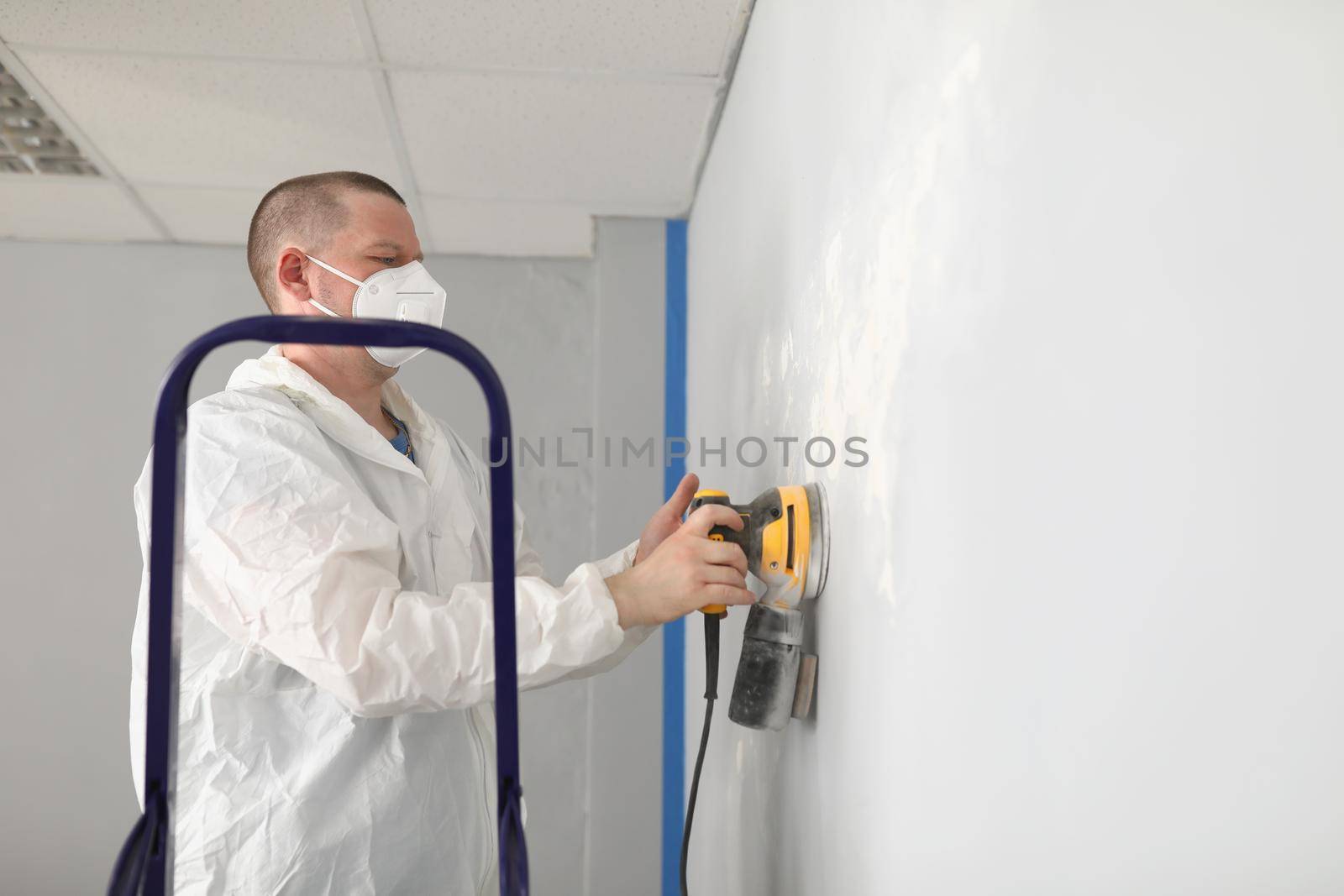 Portrait of male worker in protective costume polish wall with special equipment. Sander machine in work. Renovation, construction, interior design concept