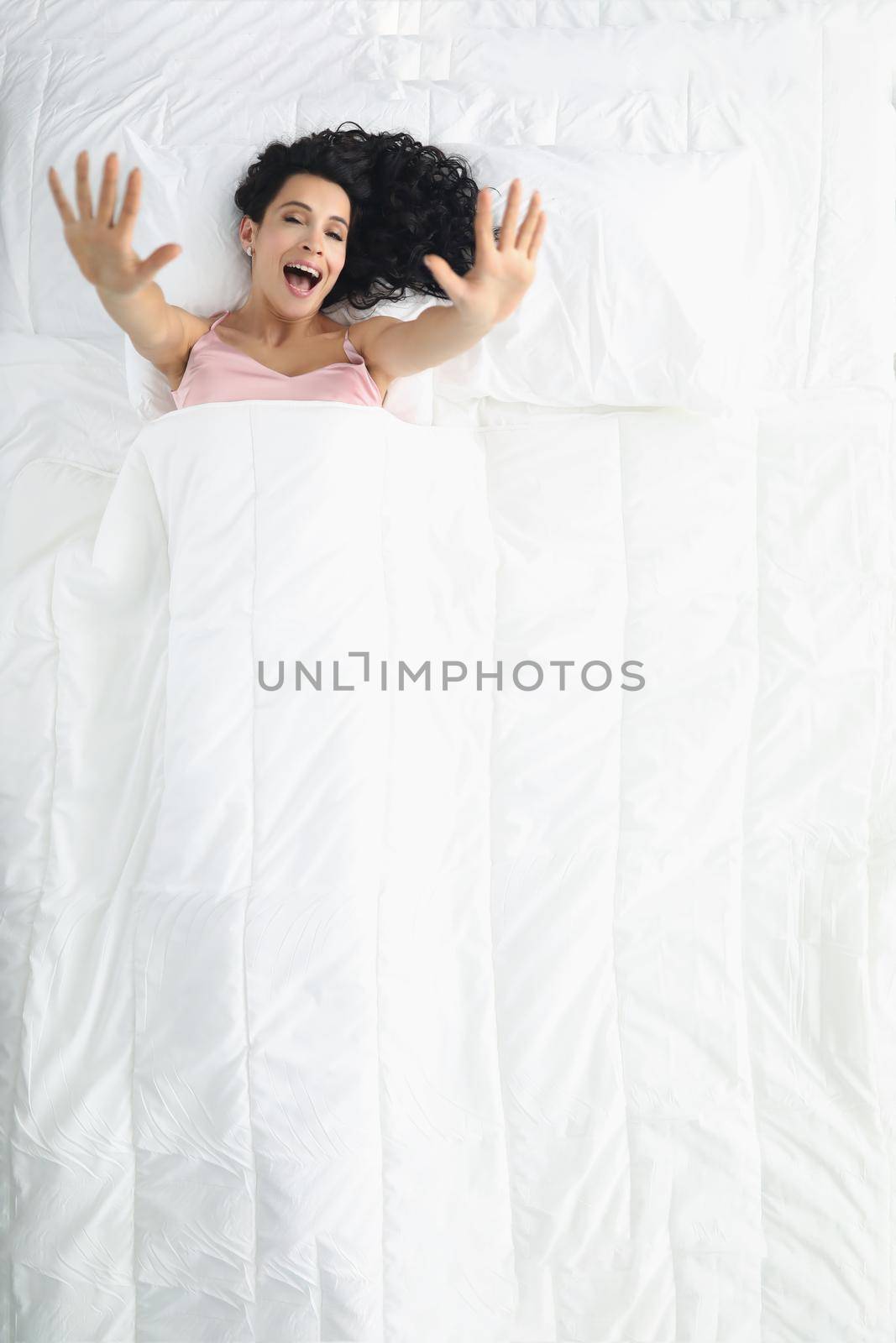 Pretty woman laying on white bedding, wake up well rested in morning, stretching after sleep by kuprevich