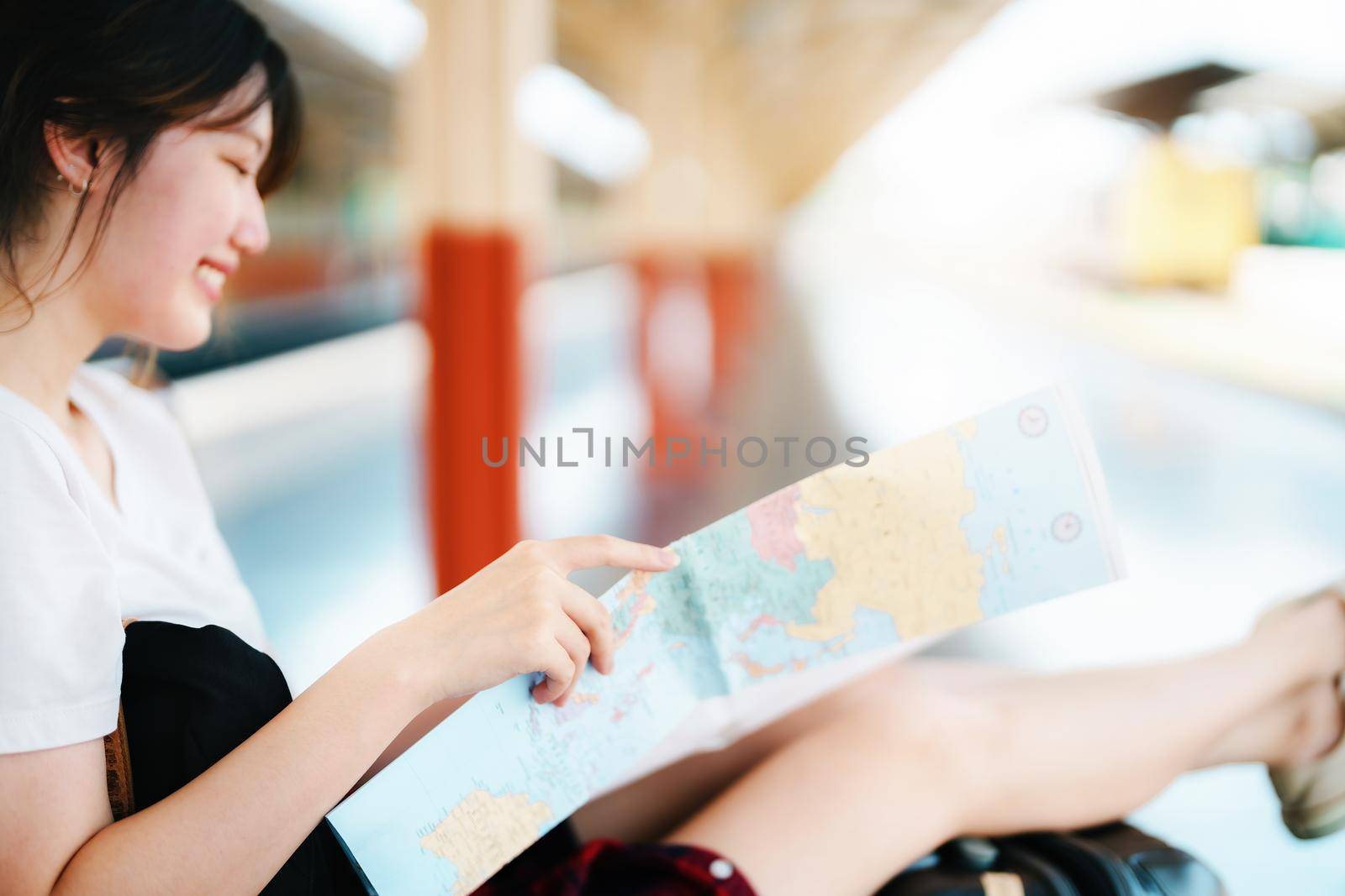 summer, relax, vacation, travel, portrait of a cute Asian girl looking at a map to plan a trip while waiting at the train station