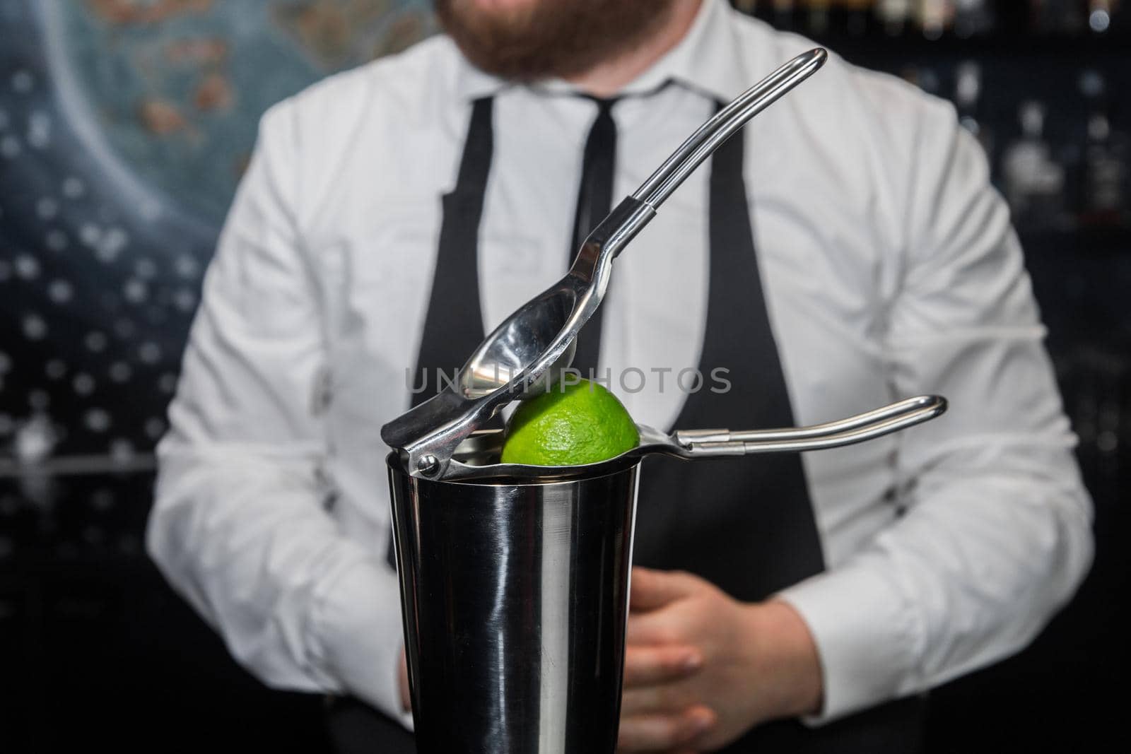 Professional bartender squeeze lime juice with an iron tool with a juicer into a metal shaker, close-up.