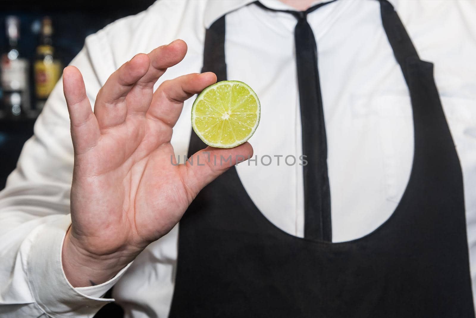 The hand of a professional bartender holds a cut piece of lime citrus, close-up.