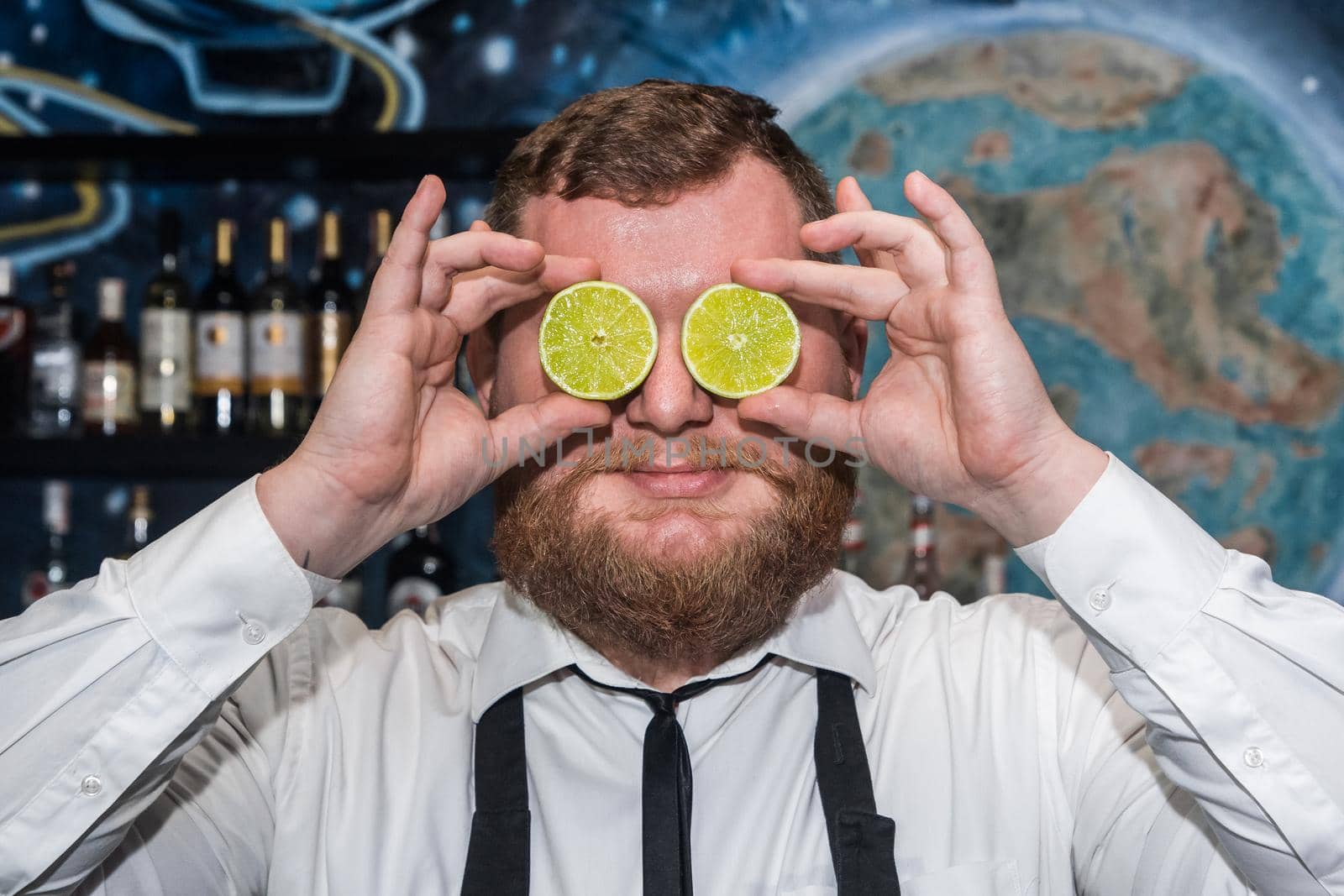 Adult funny bearded positive man professional bartender holds halves of sliced lime in his hands at the face by AYDO8