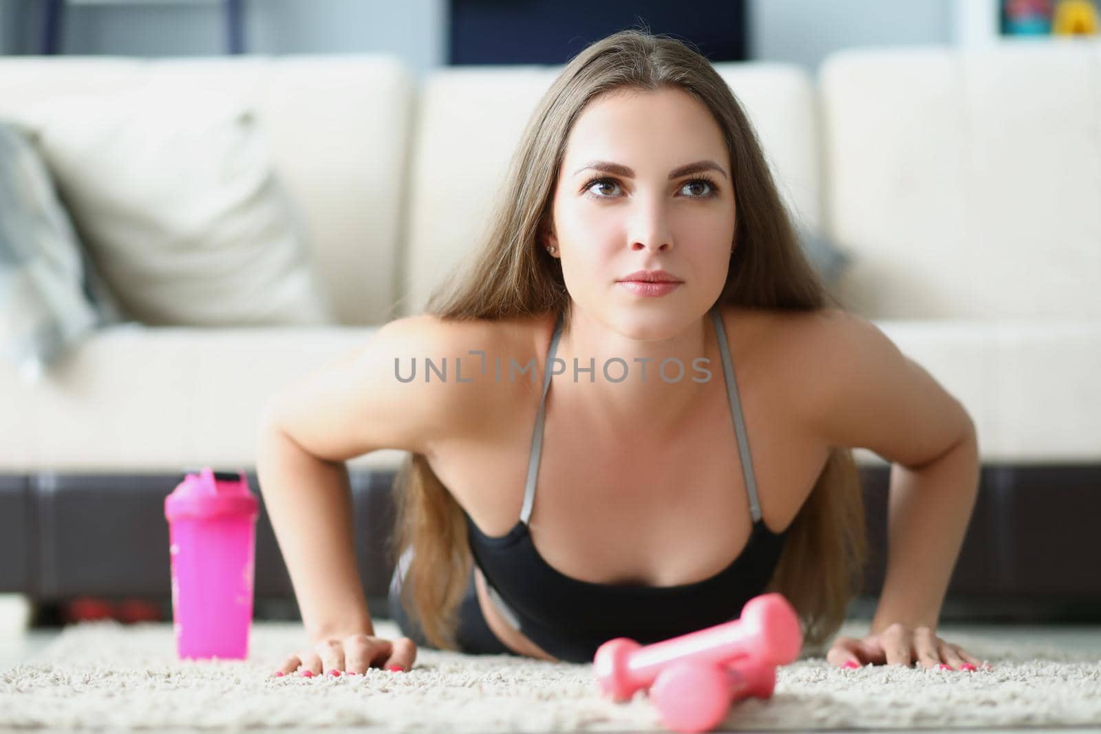 Portrait of female exercise on floor at home, doing push ups in sportswear. Lady train body with dumbbells. Sport, healthcare, physical activity concept