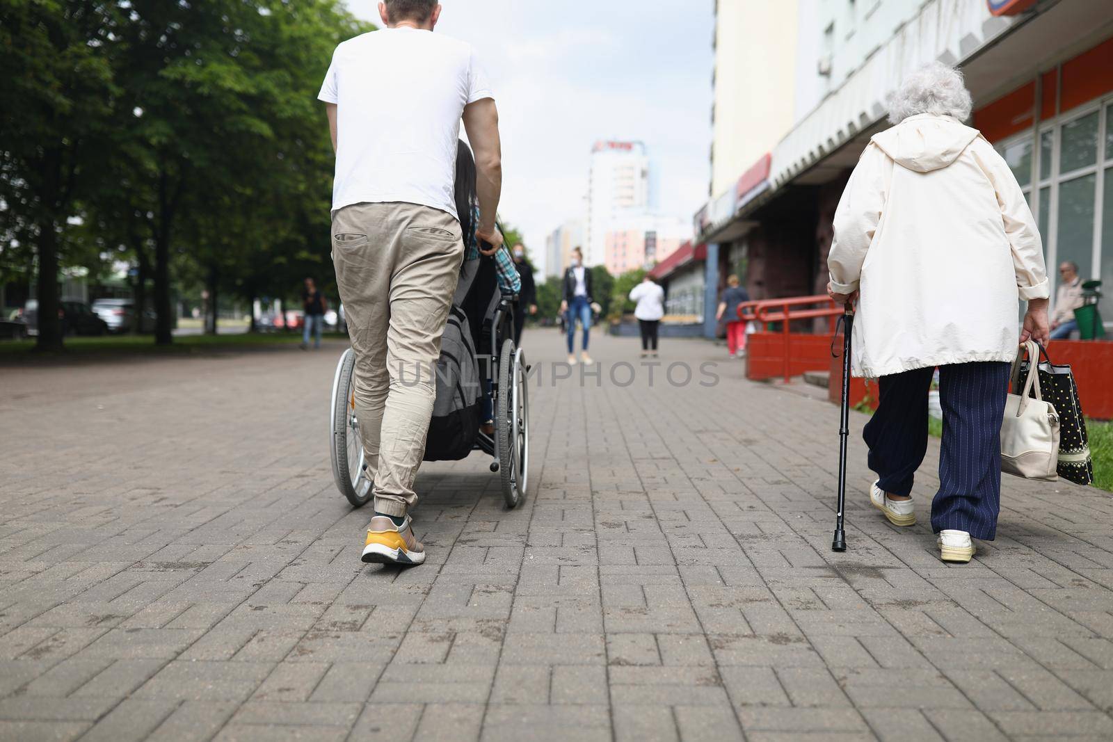 Low angle of man driving disabled woman in wheelchair across street, walking, shopping. Caregiver take care of patient. Accident, recovery, support concept