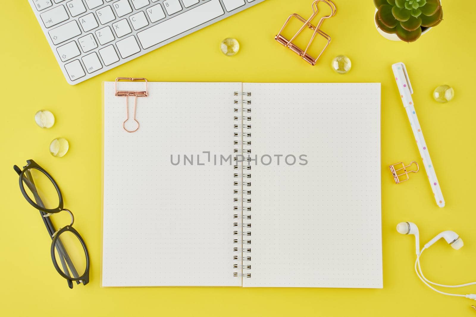 Blank notepad page in bullet journal on bright yellow office desktop. Top view of modern bright table with notebook, stationery. Mock up, copy space, concept for diary, above