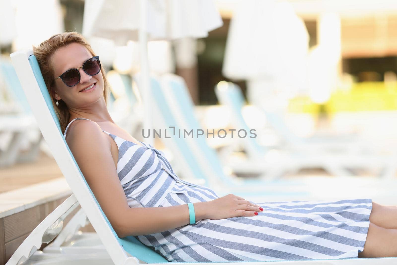 Portrait of relaxed young woman on sunbed in pretty summer dress, chilling female in sunglasses enjoy summertime. Summer, chill, leisure, vacation concept
