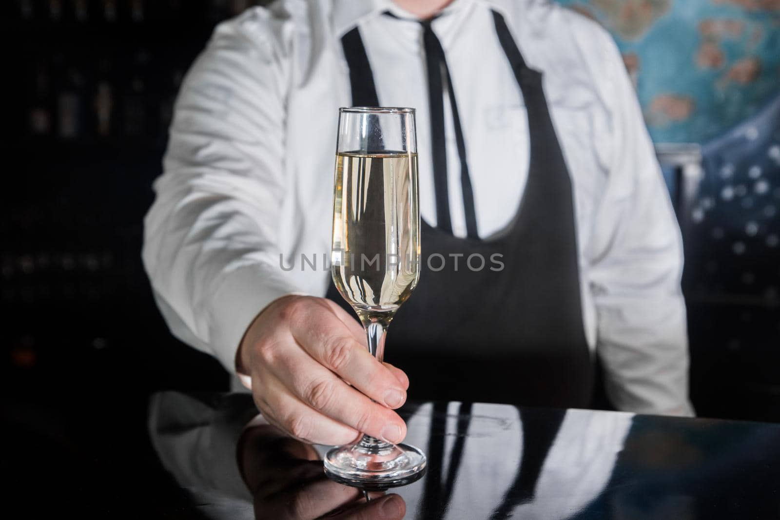 A professional bartender serves chilled champagne sparkling with gases in glass on the bar.