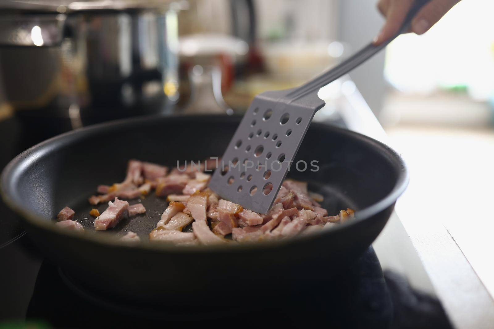 Close-up of chef stir ham or bacon slices on hot pan, person frying meat for breakfast or dinner. Cooking homemade food at home. Cooking, recipe concept