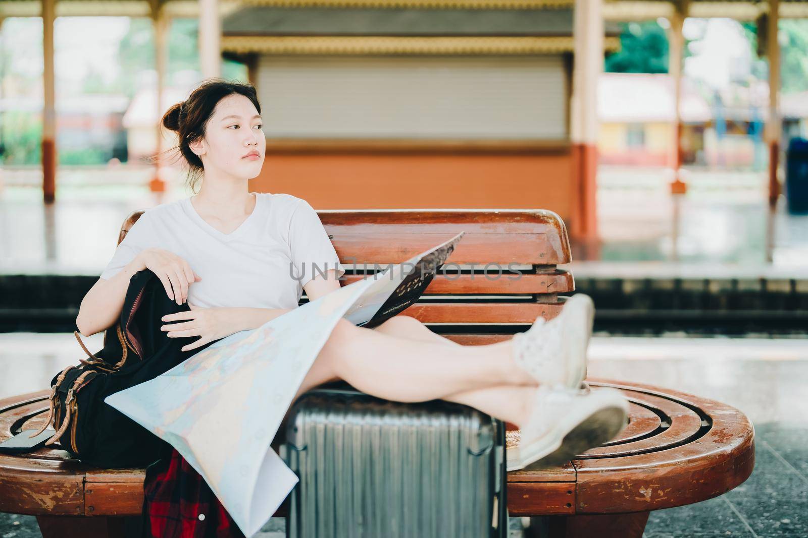 summer, relax, vacation, travel, portrait of a cute Asian girl looking at a map to plan a trip while waiting at the train station