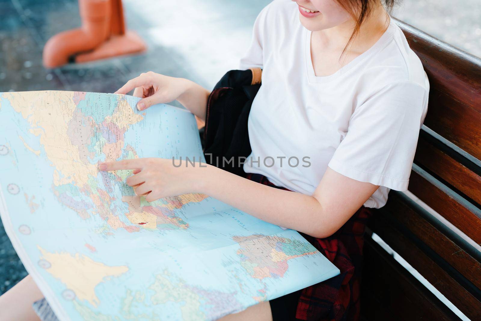 summer, relax, vacation, travel, portrait of a cute Asian girl looking at a map to plan a trip while waiting at the train station