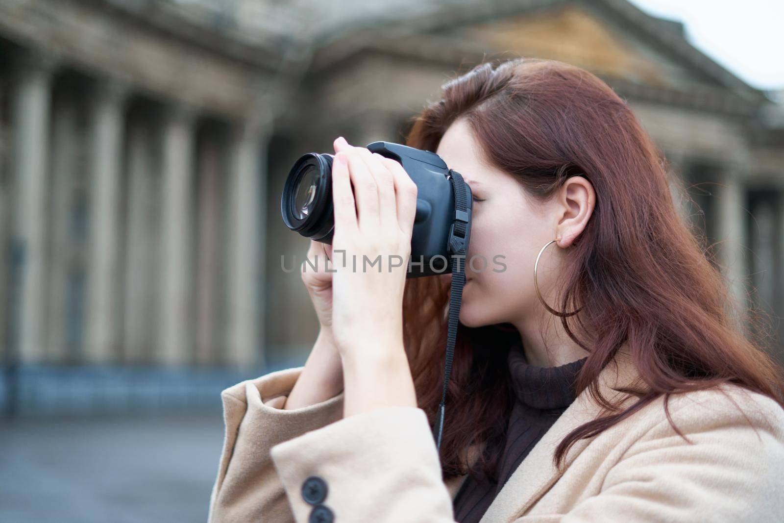 Beautiful stylish fashionable girl holds camera in her hands and takes pictures. Woman photographer with long dark hair in city, urban shoot. Unrecognizable person, side view