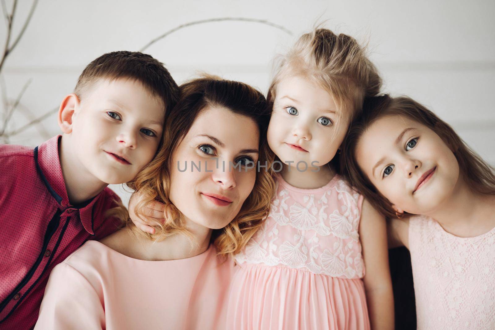 Portrait of cute family looking at camera and smiling at home. Young attractive mother posing with son and cute daughters. Lovely family hugging each other. Concept of love and motherhood.