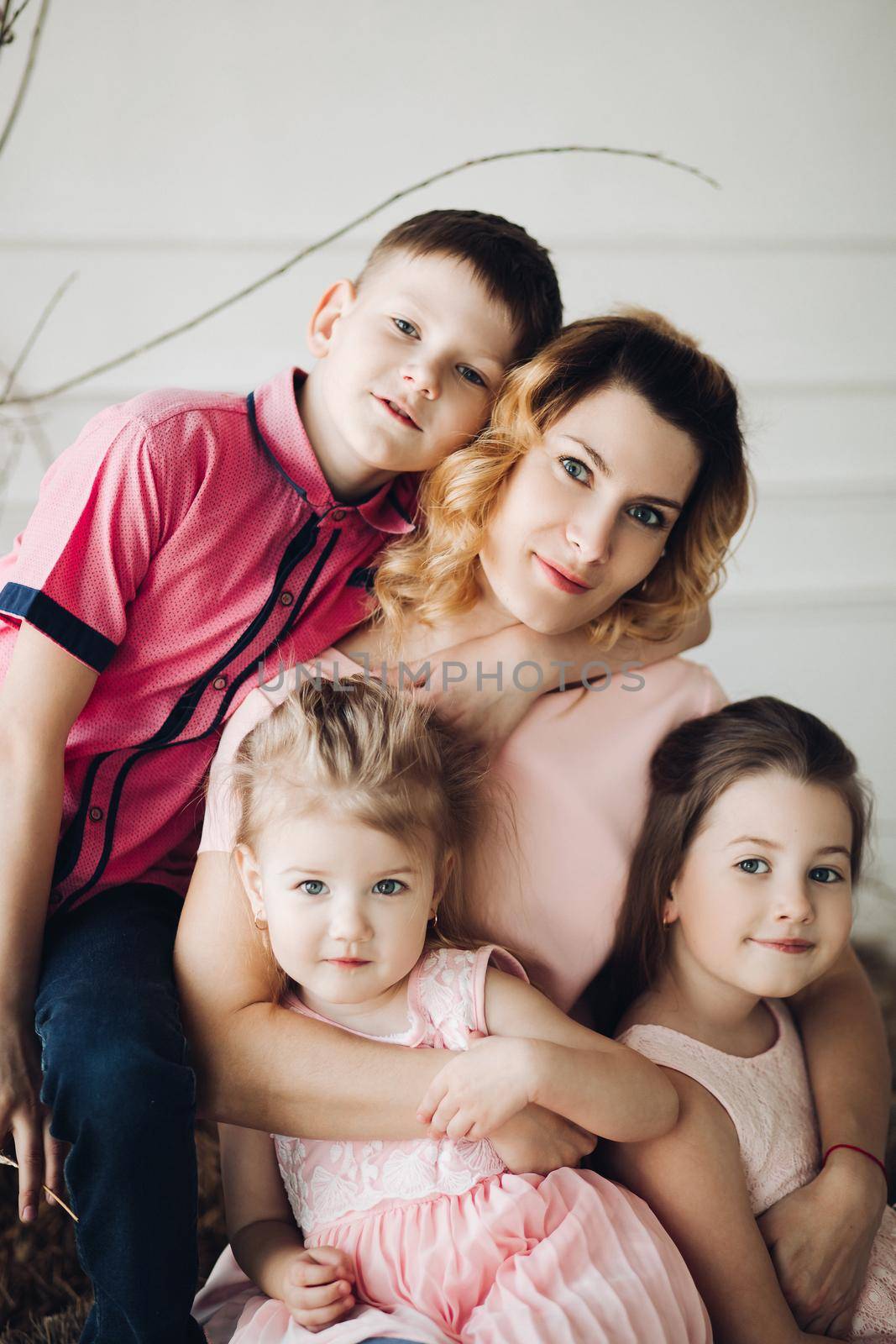 Portrait of cute family looking at camera and smiling at home. Young attractive mother posing with son and cute daughters. Lovely family hugging each other. Concept of love and motherhood.