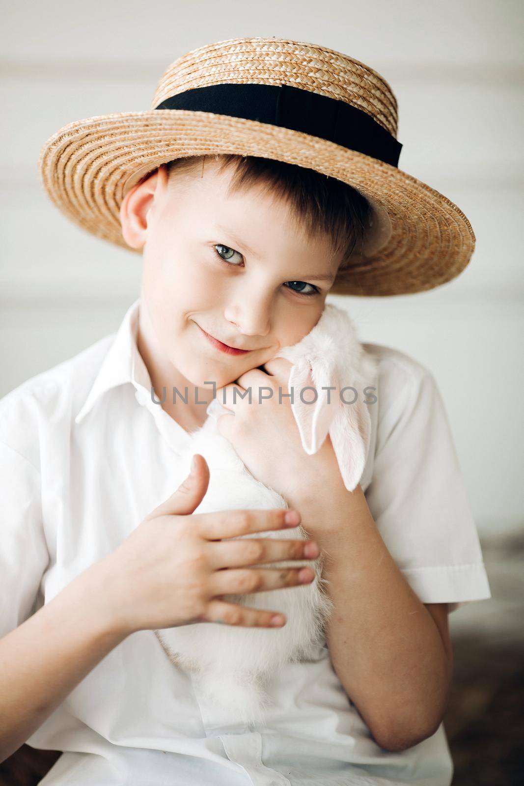 Boy in hay hat keeping cute white bunny and smiling by StudioLucky