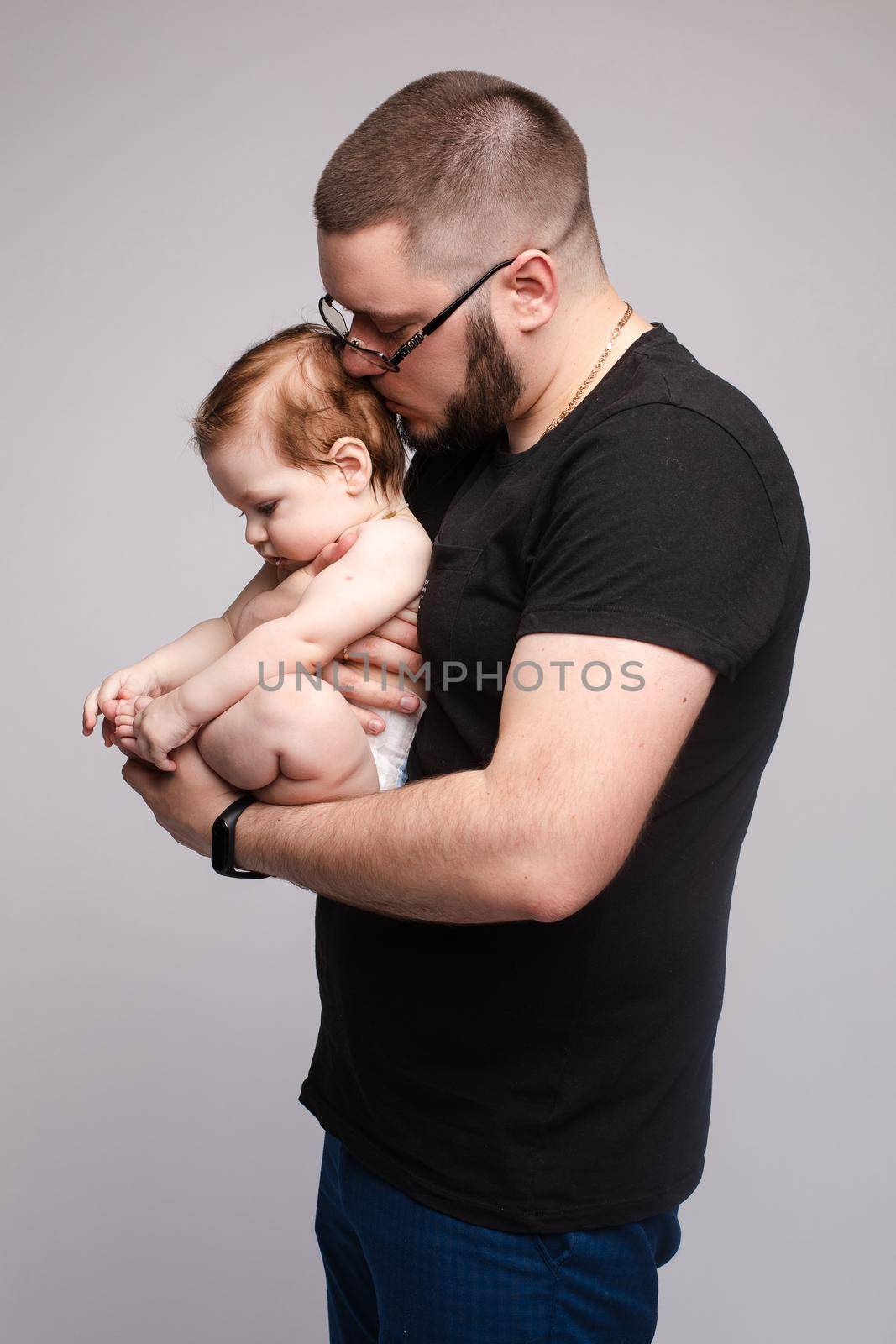 Father keeping little baby in hands and kissing kid by StudioLucky