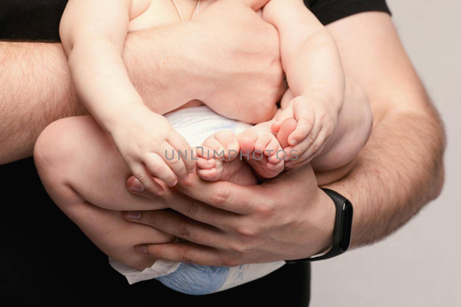 Side view of lovely father keeping little baby in hands and kissing kid on grey isolated background in studio. Happy male parent hugging and playing with child. Concept of family and love.