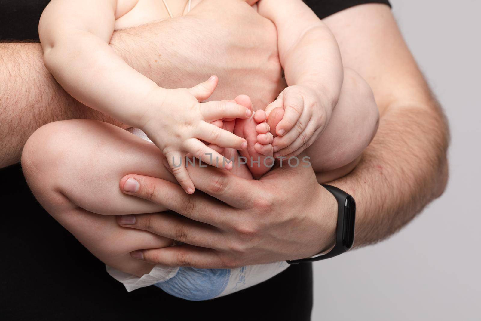 Side view of lovely father keeping little baby in hands and kissing kid on grey isolated background in studio. Happy male parent hugging and playing with child. Concept of family and love.