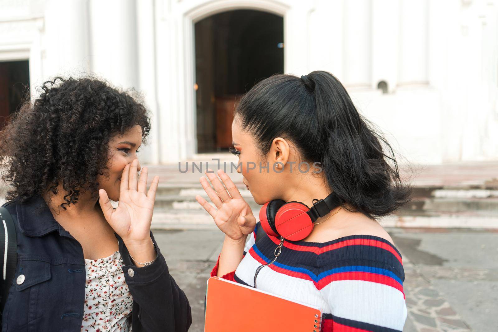 Two young latin women multiracial university students gossiping and talking about their secrets in the central park of the city of Leon Nicaragua