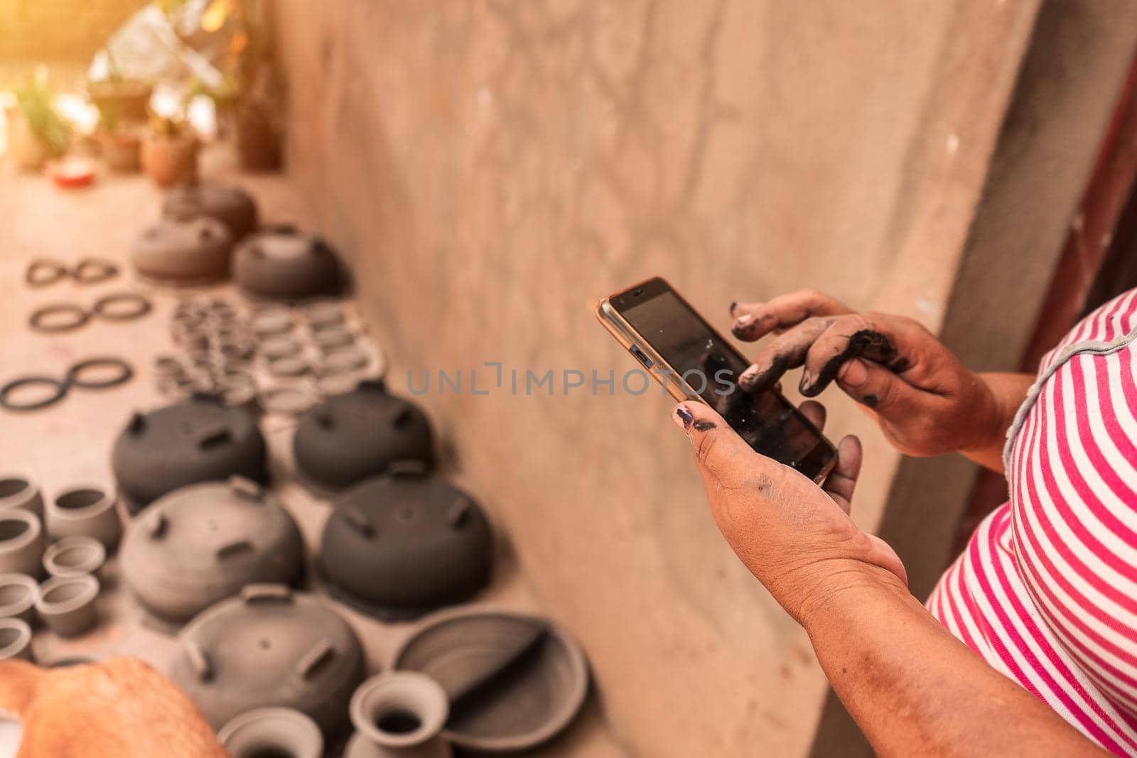 Artisan checking her cell phone to make online sales while her clay pots dry in the sun at a workshop in La Paz Centro, Nicaragua. Concept of travel, culture and economy in poor countries of America.