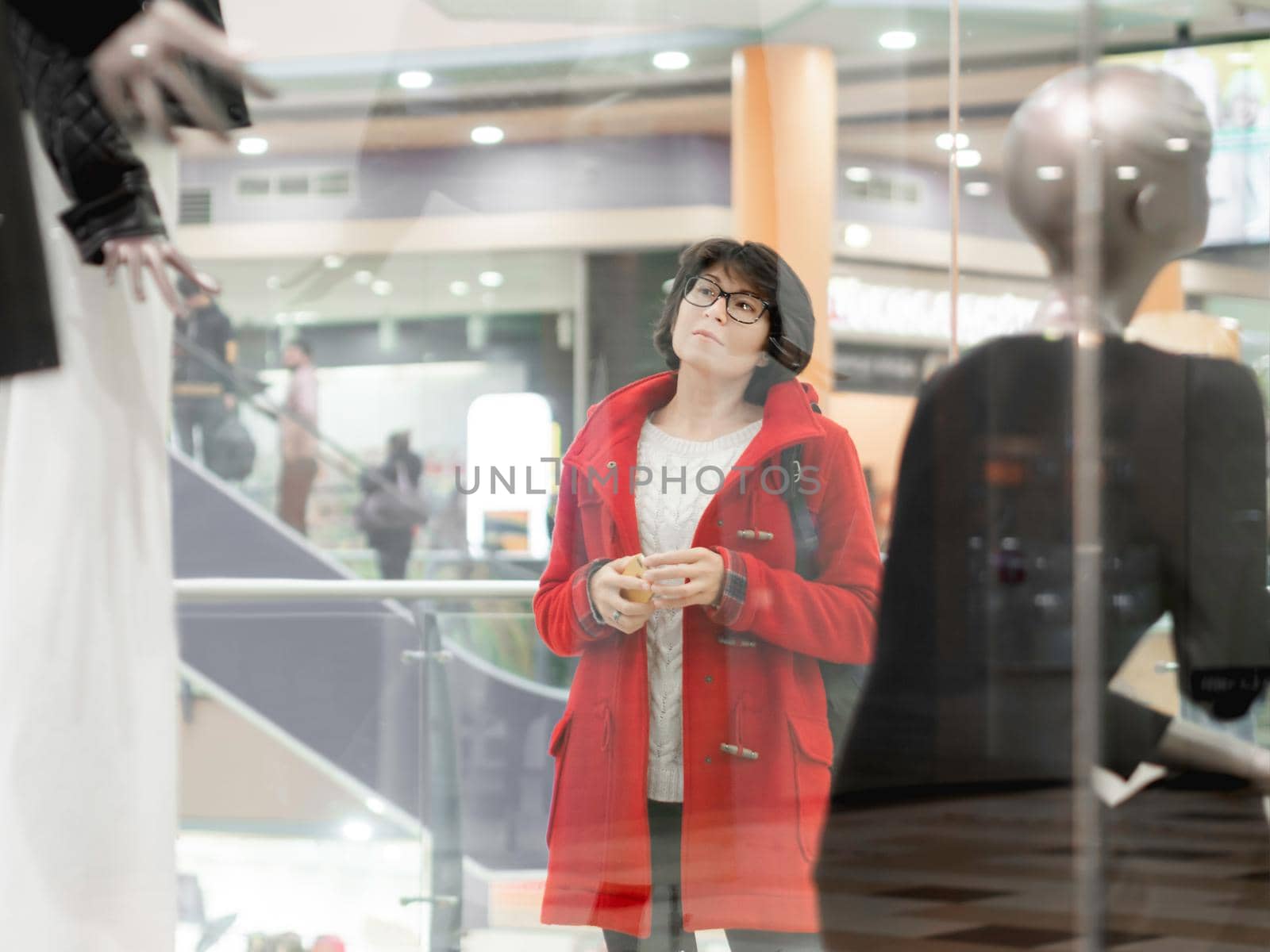 Woman stares on dummies in clothing store. Casual outfit hanging on mannequins. View through transparent shop window. Shopping at mall. Basic clothes for everyday wear. Modern urban fashion. by aksenovko