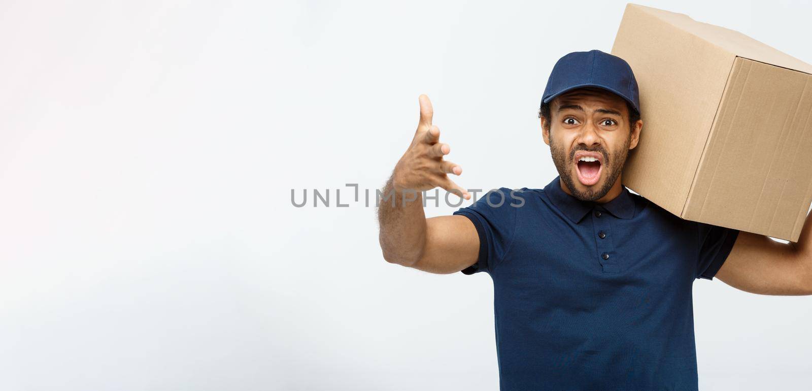 Delivery Concept - Portrait of Serious African American delivery man showing silly aggressive expression with holding a box package. Isolated on Grey studio Background. Copy Space