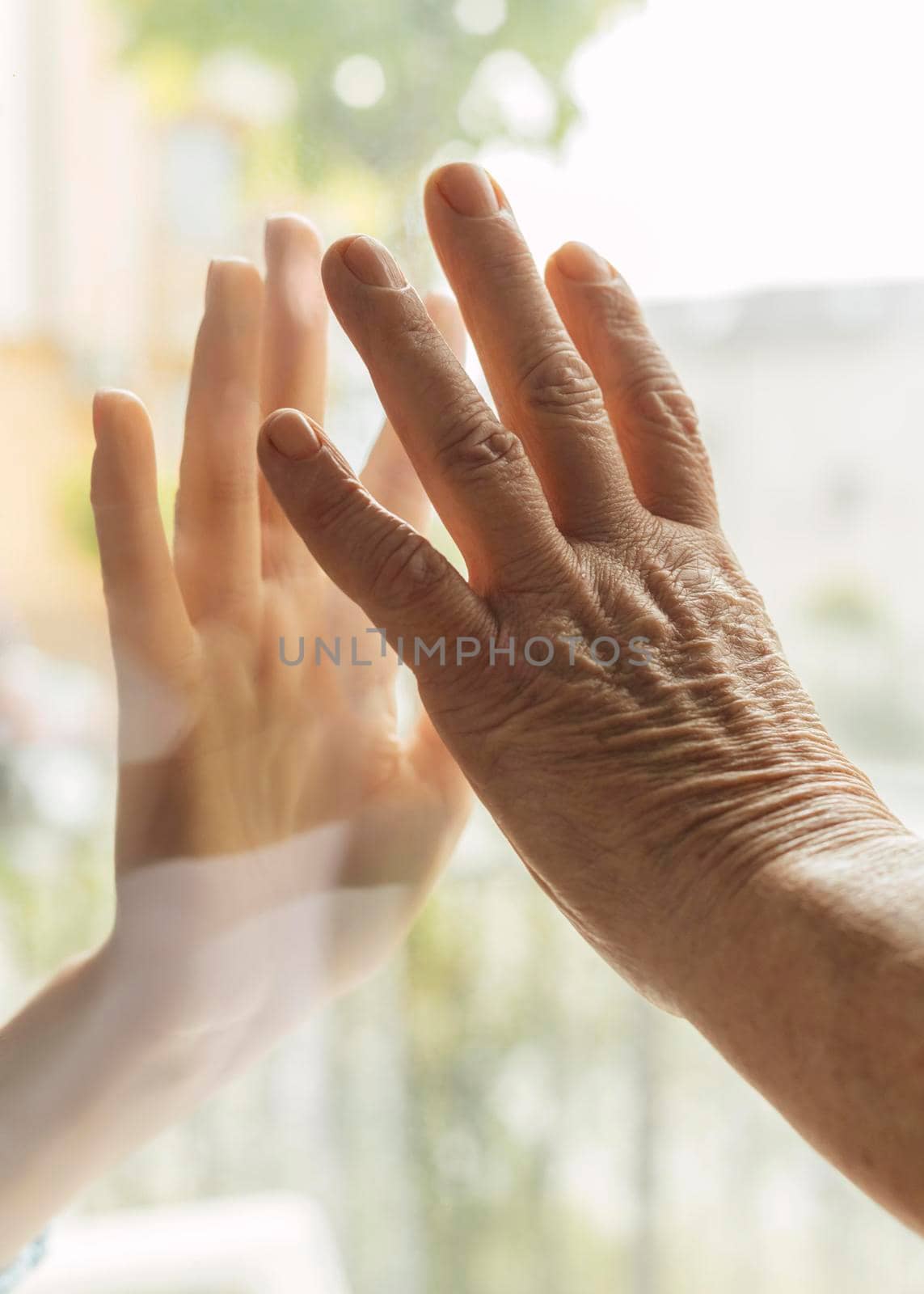 elder woman touching hand with someone through window during pandemic