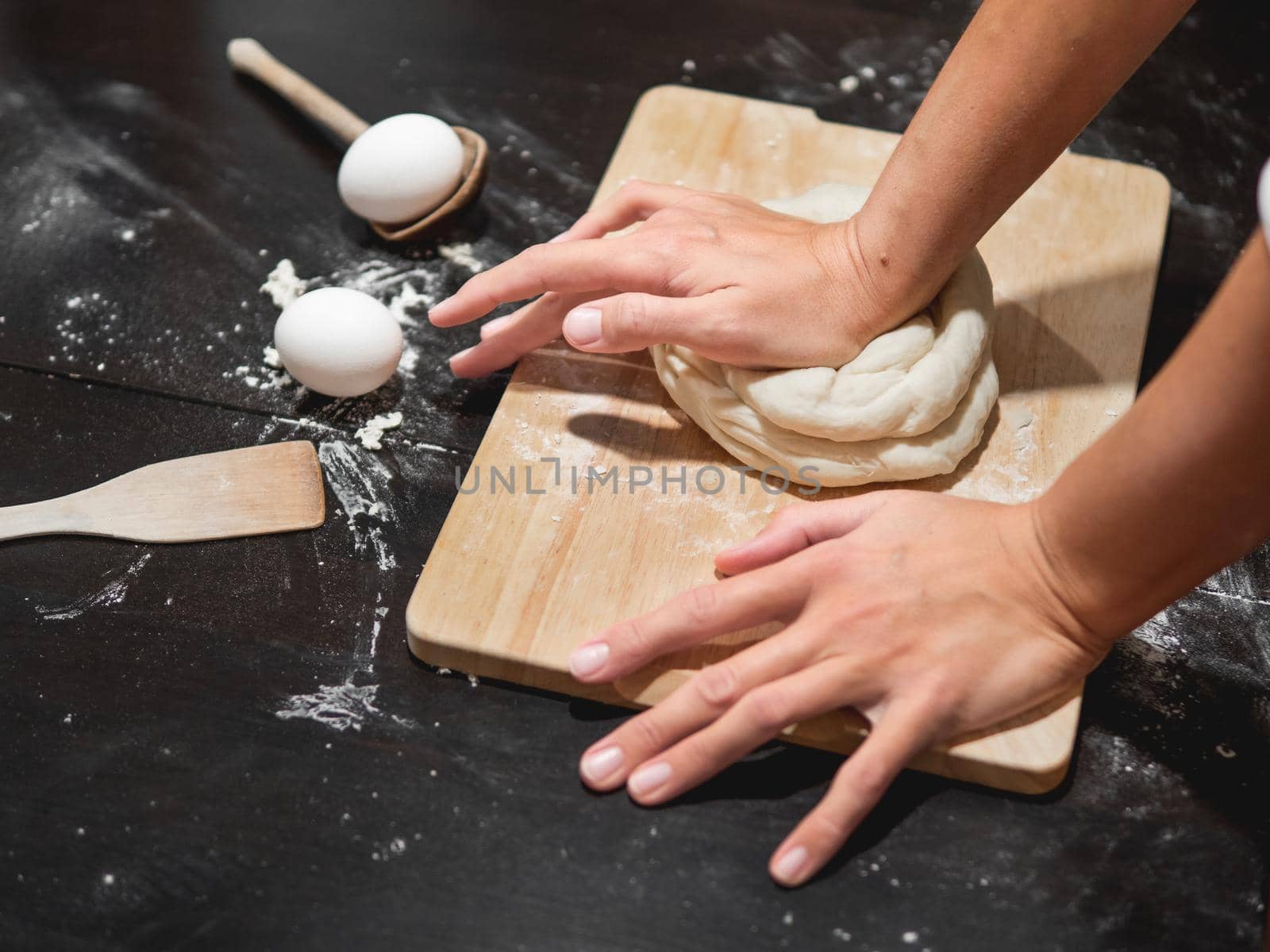 Woman kneads dough with flour and eggs on black wooden table. Cooking at home.