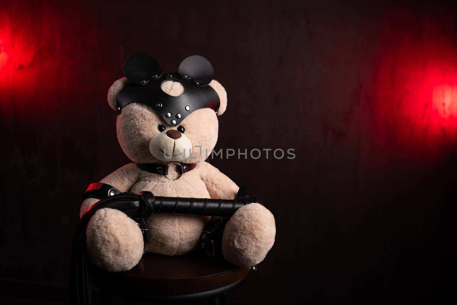 a toy teddy bear with a whip, dressed in leather belts and a mask, an accessory for BDSM games on a dark red texture background by Rotozey