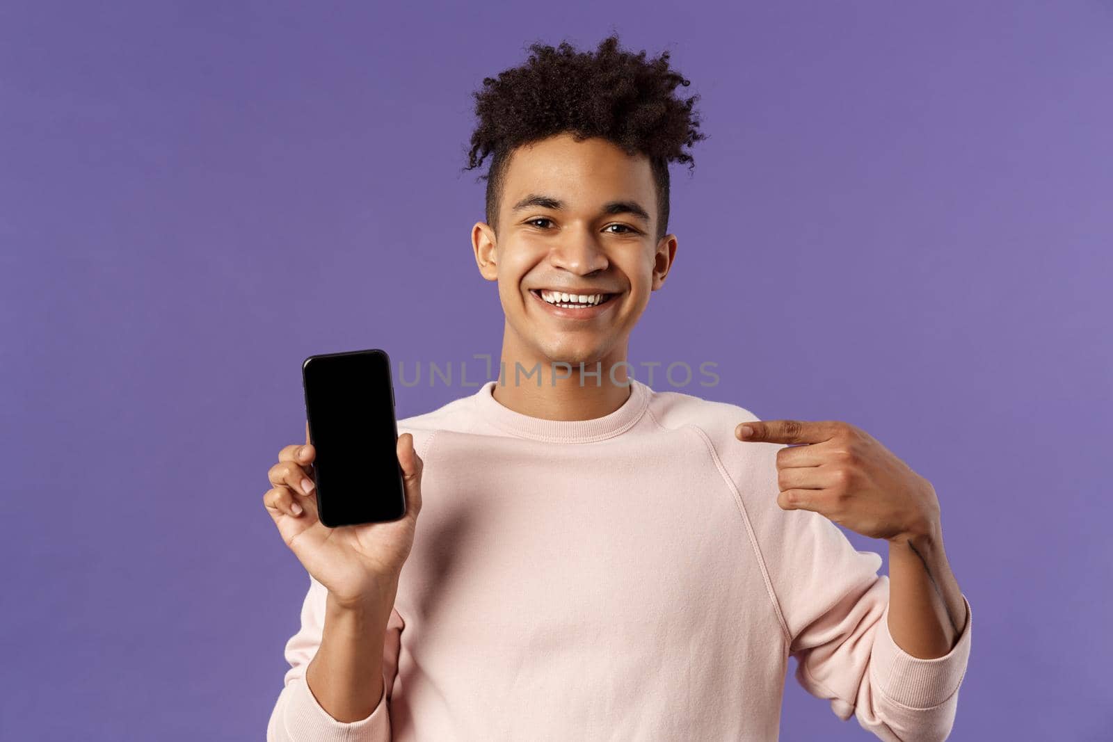 Close-up portrait of young handsome man promoting smartphone app or shopping online, internet delivery for goods, holding mobile phone pointing at display and smiling pleased, recommend.