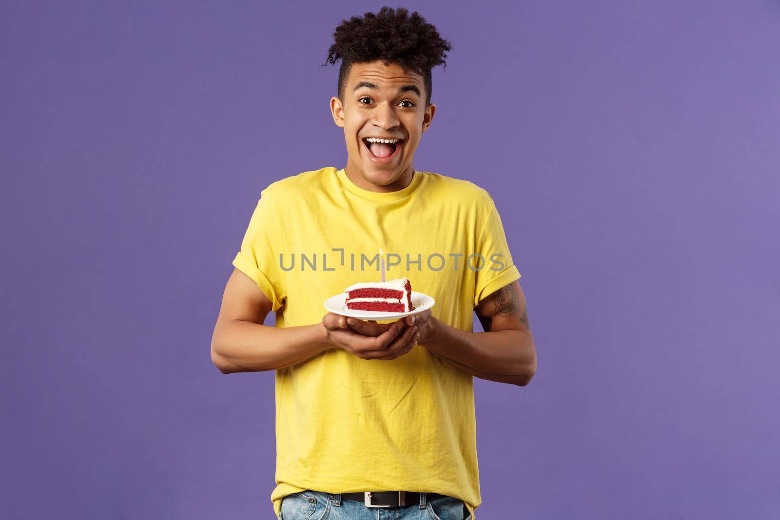 Happy birthday to me. Portrait of upbeat, excited hispanic man with dreads celebrating b-day, holding plate cake with lit candle, smiling amused, making wish, purple background.