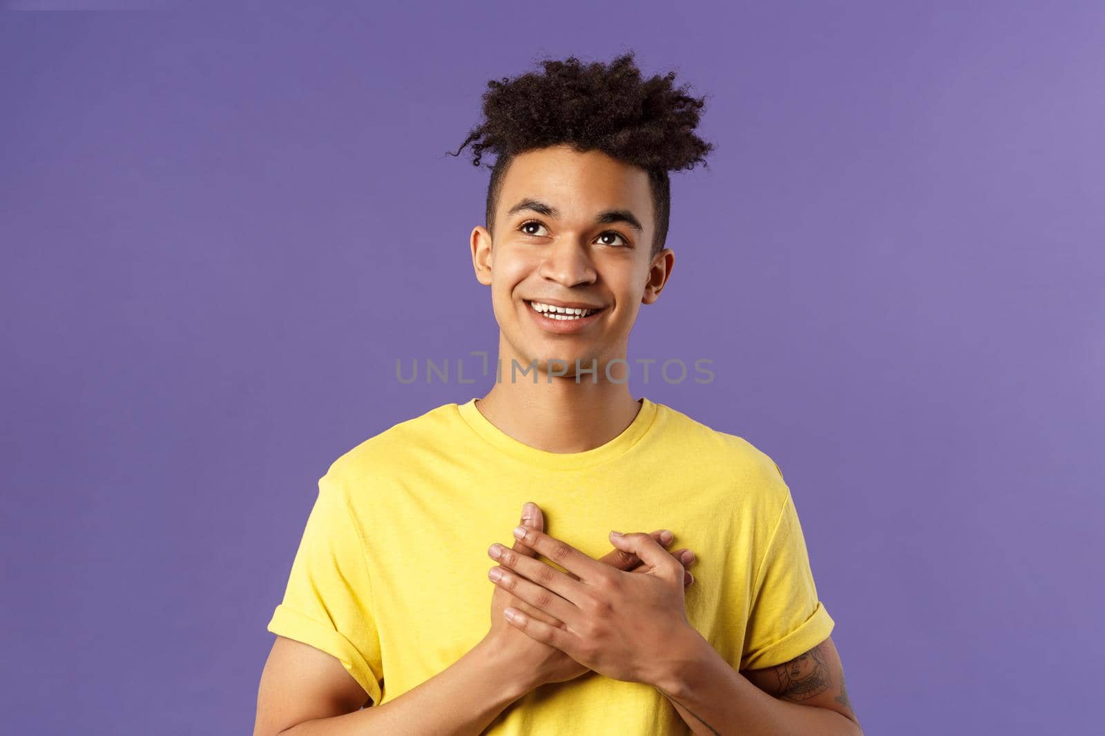 Close-up portrait of touched, romantic attractive man, hold hands on heart, remember nice lovely memory, looking up daydreaming, smiling pleased, appreciate something, purple background.