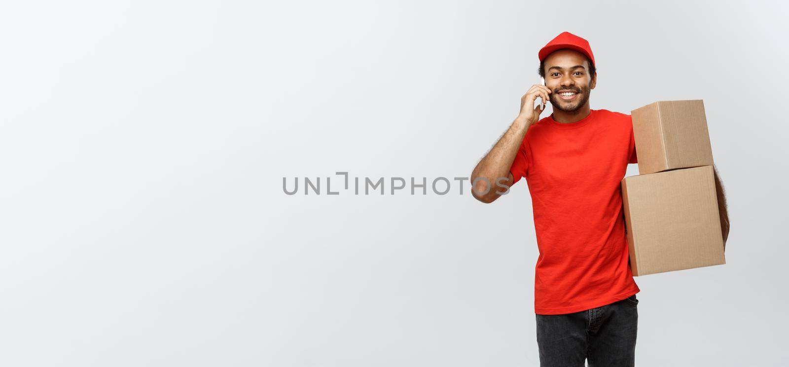 Delivery Concept - Portrait of Handsome African American delivery man or courier with box calling phone to customer. Isolated on Grey studio Background. Copy Space