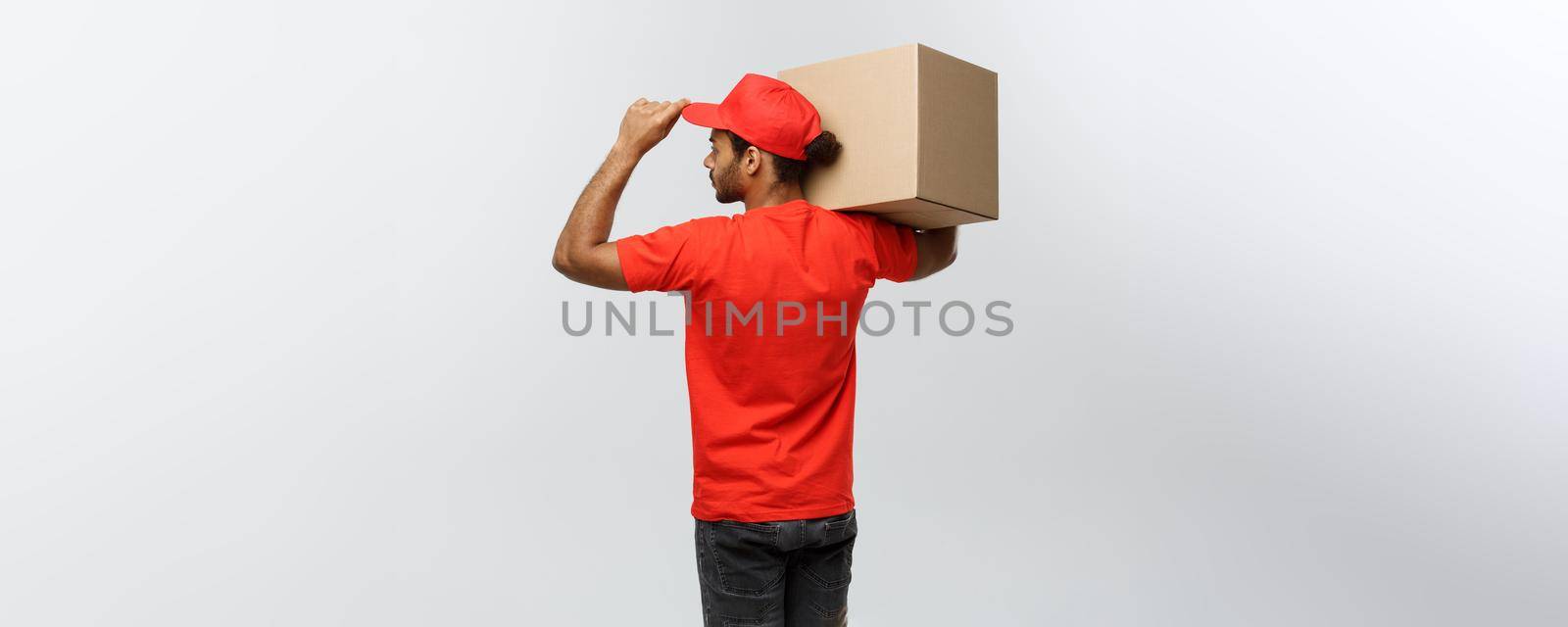 Delivery Concept - back view of Handsome African American delivery man with box package. Isolated on Grey studio Background. Copy Space. by Benzoix