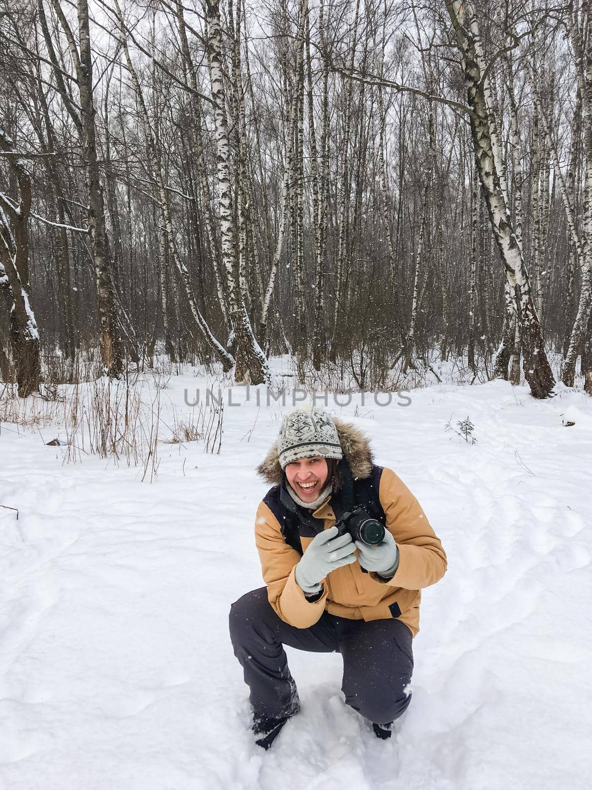 Smiling man with camera in winter forest. Photographer takes pictures of trees under snow. Leisure activity in cold season. by aksenovko