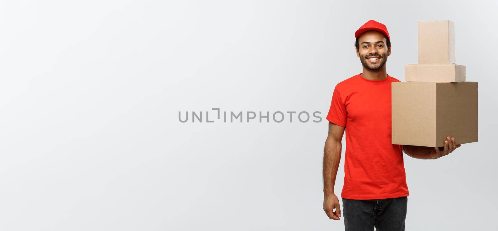 Delivery Concept - Portrait of Happy African American delivery man in red cloth holding a box package. Isolated on Grey studio Background. Copy Space