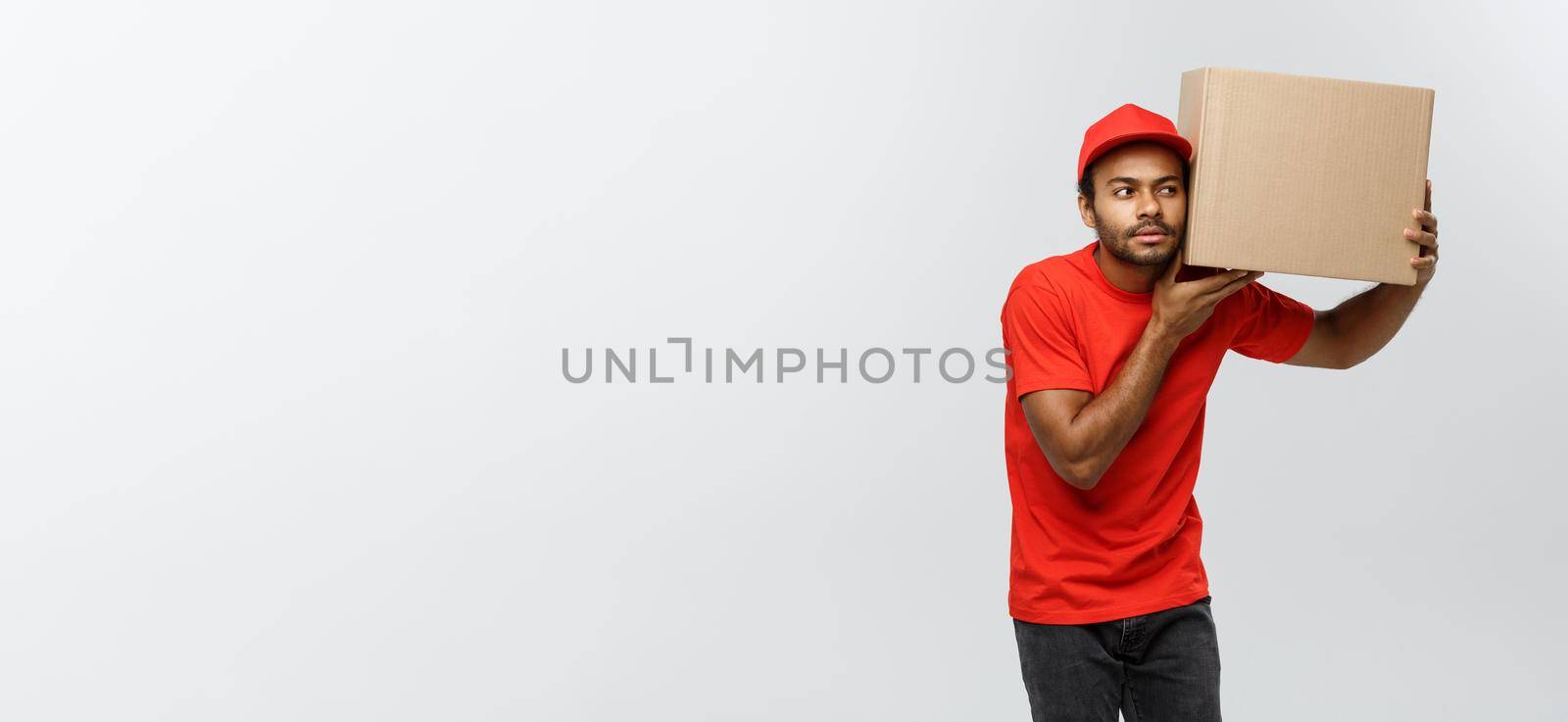 Delivery Concept - Portrait of Curious African American delivery man listen inside a box package. Isolated on Grey studio Background. Copy Space