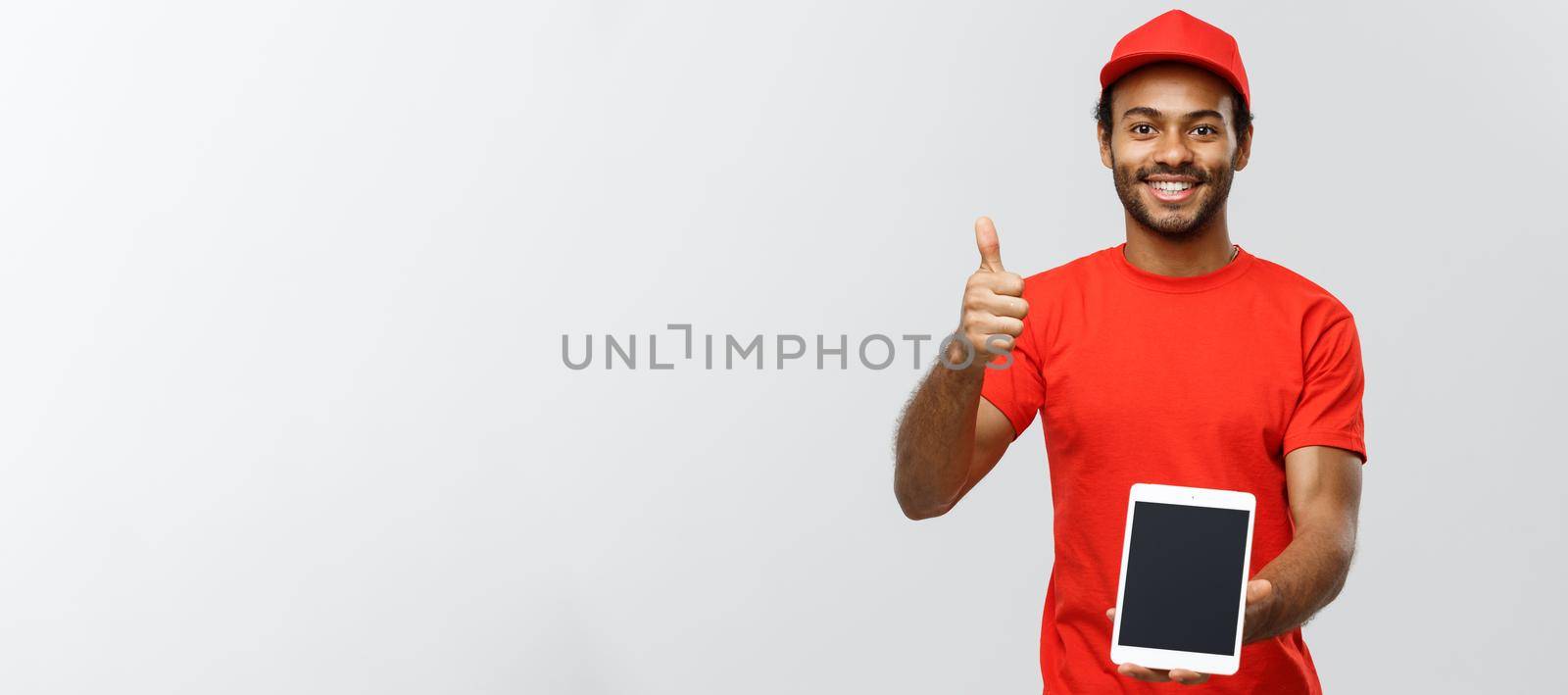 Delivery Concept - Portrait of Handsome African American delivery man or courier showing tablet on you to check the order. Isolated on Grey studio Background. Copy Space