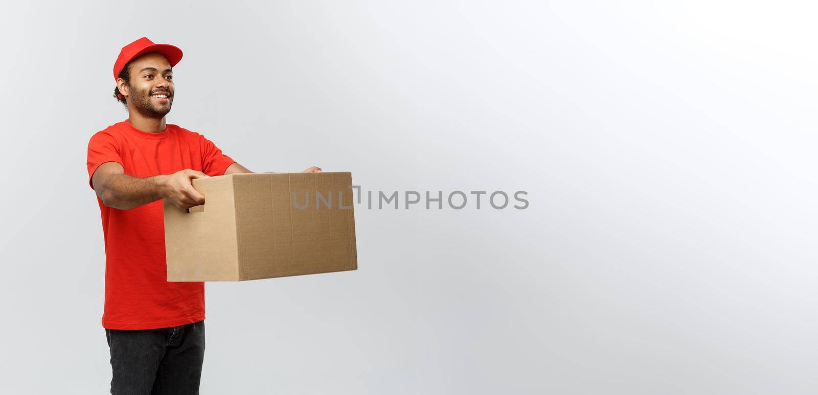 Delivery Concept - Portrait of Happy African American delivery man in red cloth holding a box package. Isolated on Grey studio Background. Copy Space