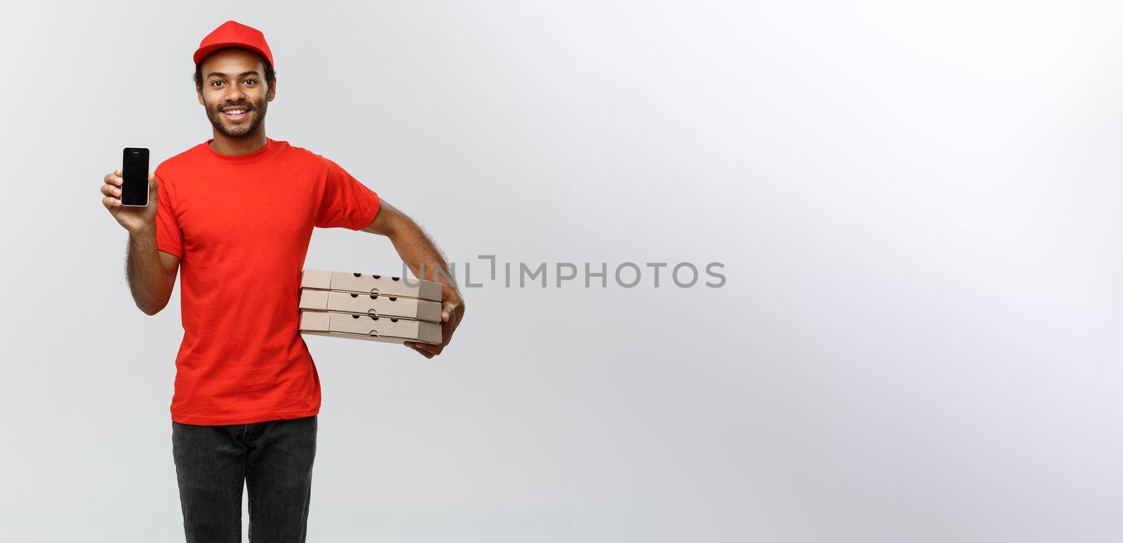 Delivery Concept - Portrait of Handsome African American delivery man or courier with pizza box showing mobile phone on you to check the order. Isolated on Grey studio Background. Copy Space