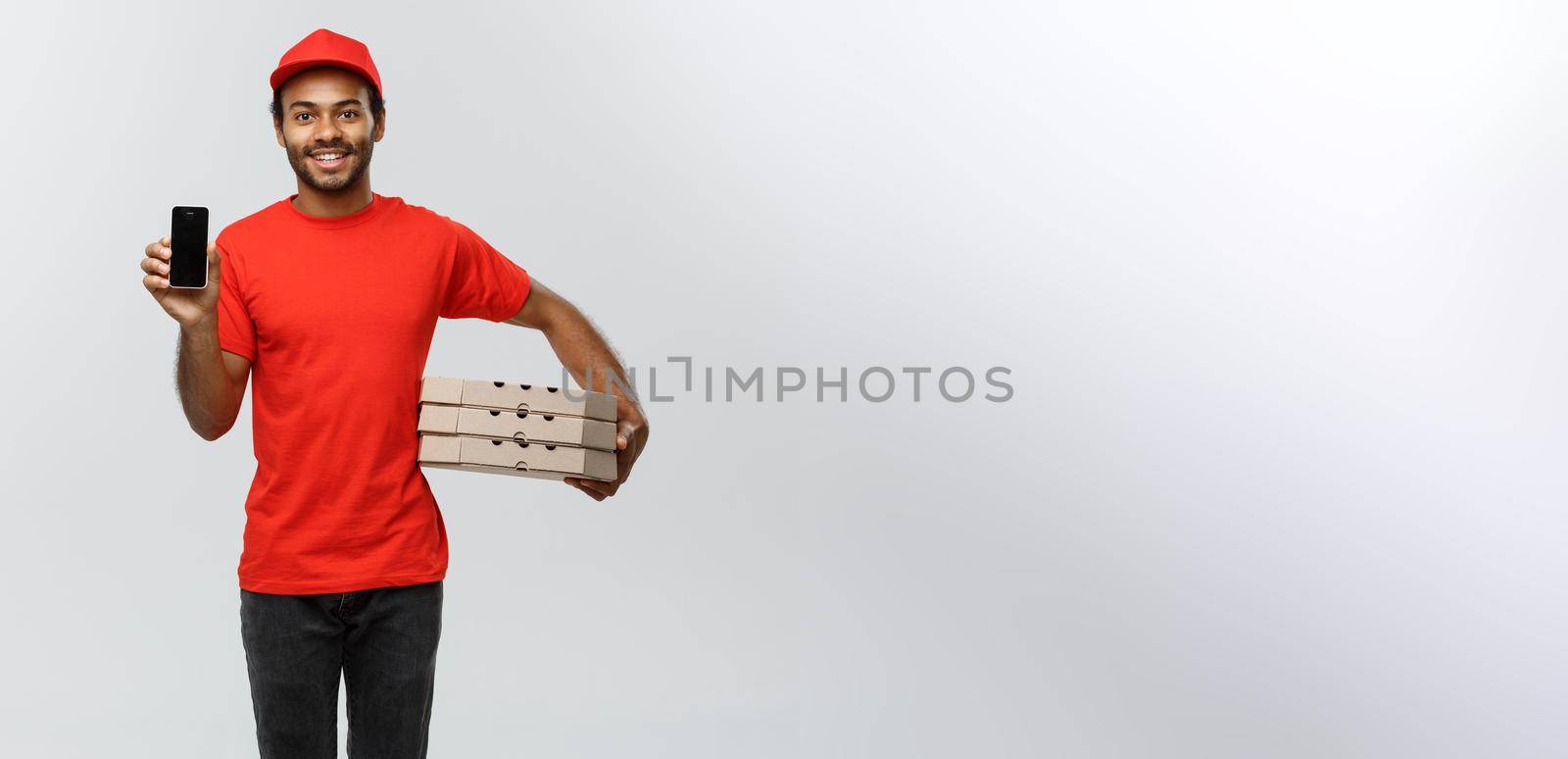 Delivery Concept - Portrait of Handsome African American delivery man or courier with pizza box showing mobile phone on you to check the order. Isolated on Grey studio Background. Copy Space. by Benzoix