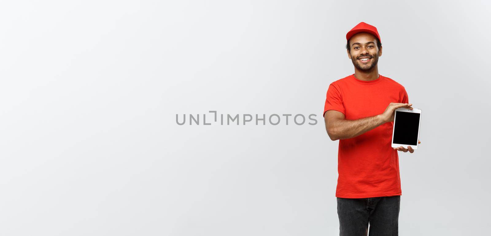 Delivery Concept - Portrait of Handsome African American delivery man or courier showing tablet on you to check the order. Isolated on Grey studio Background. Copy Space