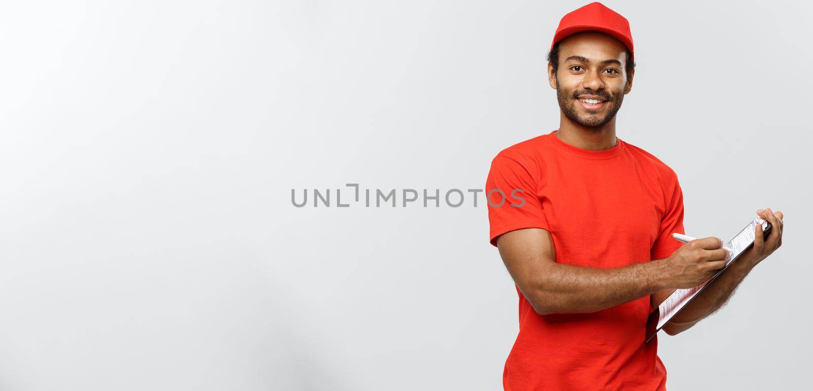 Delivery Concept - Portrait of Handsome African American delivery man or courier writing on a order document. Isolated on Grey studio Background. Copy Space. by Benzoix