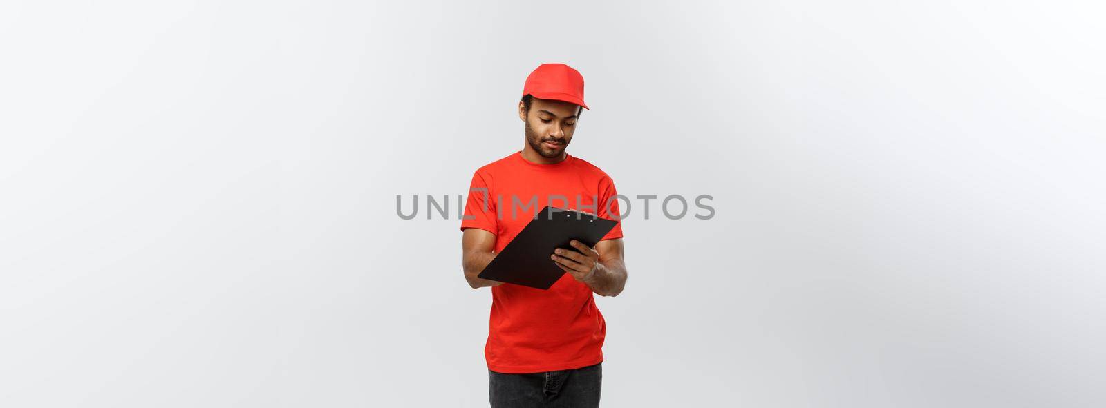 Delivery Concept - Portrait of Handsome African American delivery man or courier writing on a order document. Isolated on Grey studio Background. Copy Space. by Benzoix