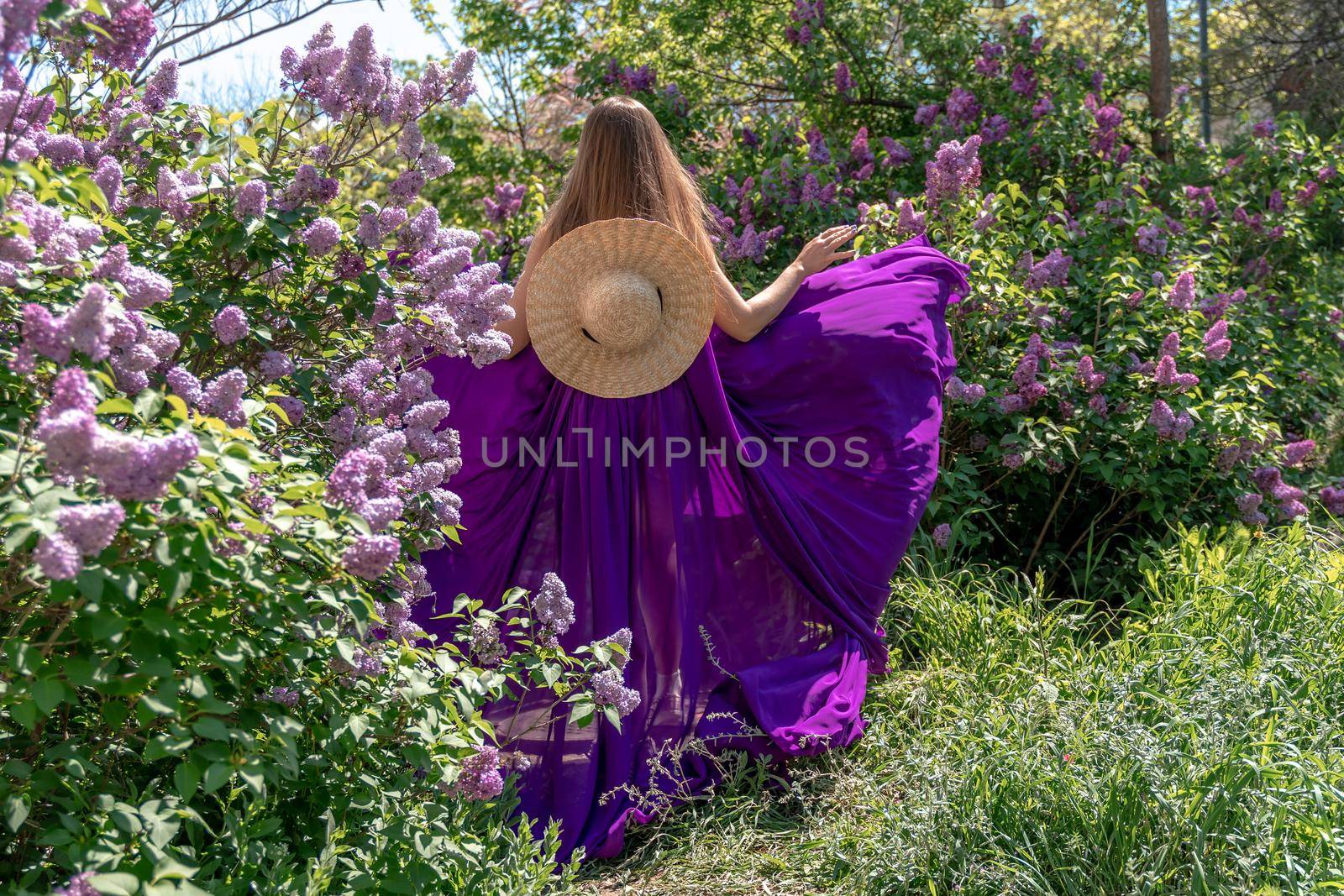 Fashion Model in Lilac Flowers, Young Woman in Beautiful Long Dress Waving on Wind, Outdoor Beauty Portrait in Blooming Garden.