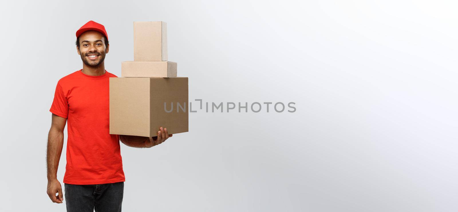 Delivery Concept - Portrait of Happy African American delivery man in red cloth holding a box package. Isolated on Grey studio Background. Copy Space