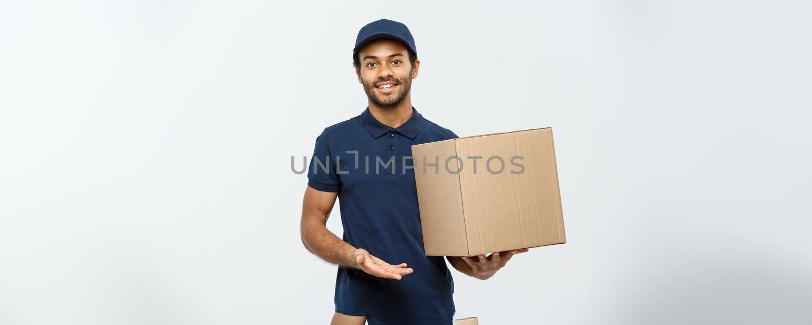 Delivery Concept - Portrait of Happy African American delivery man pointing hand to present a box package. Isolated on Grey studio Background. Copy Space. by Benzoix